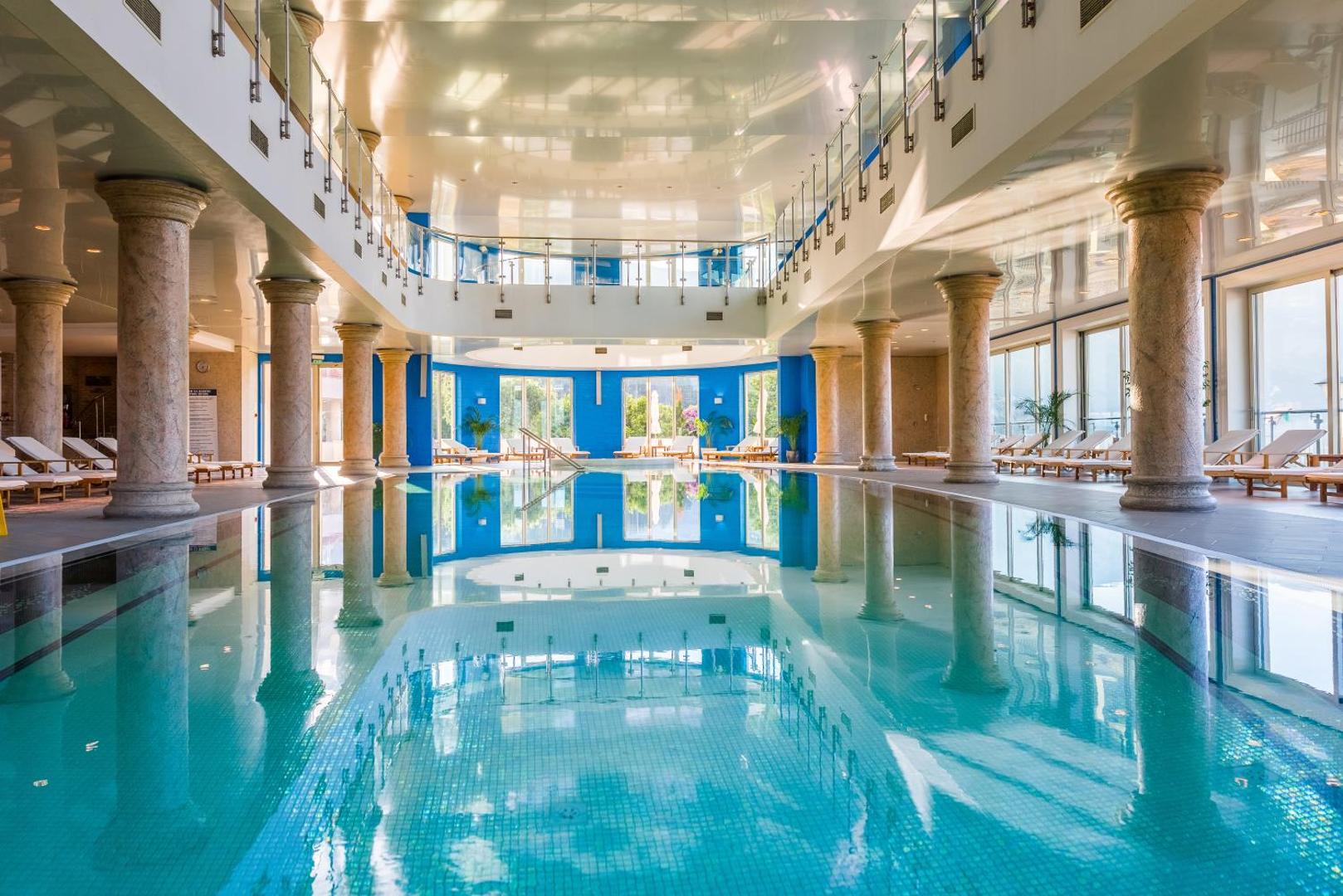 Splendid Conference & Spa Resort plašais iekštelpu baseins ar kolonnām un stikla margu balkonu — gaiša un moderna spa zona