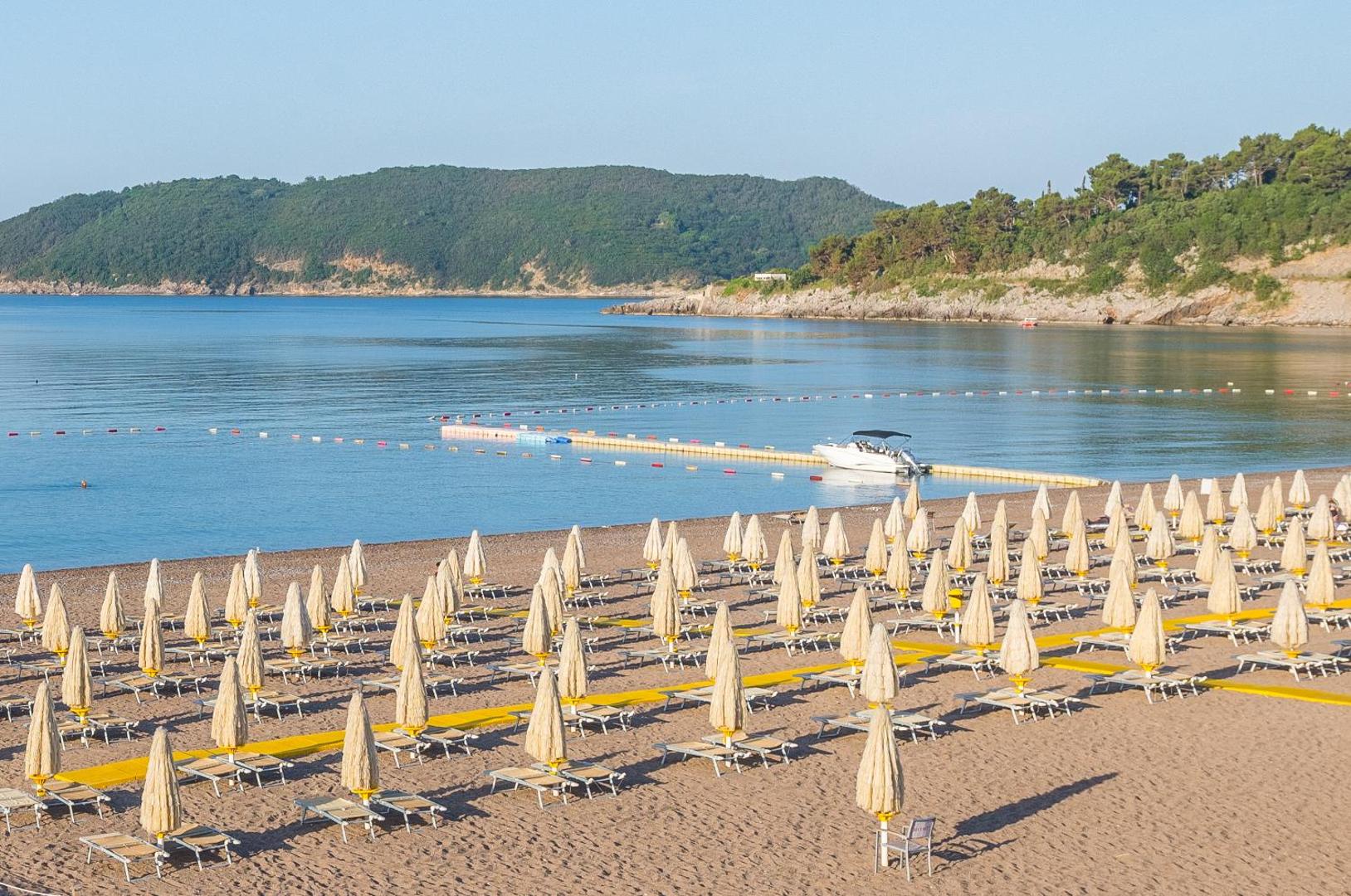 Splendid Conference & Spa Resort privātā pludmale Bečiči kūrortā Melnkalnē — skats uz Adrijas jūru ar saulessargiem, sauļošanās krēsliem un laivu piestātni
