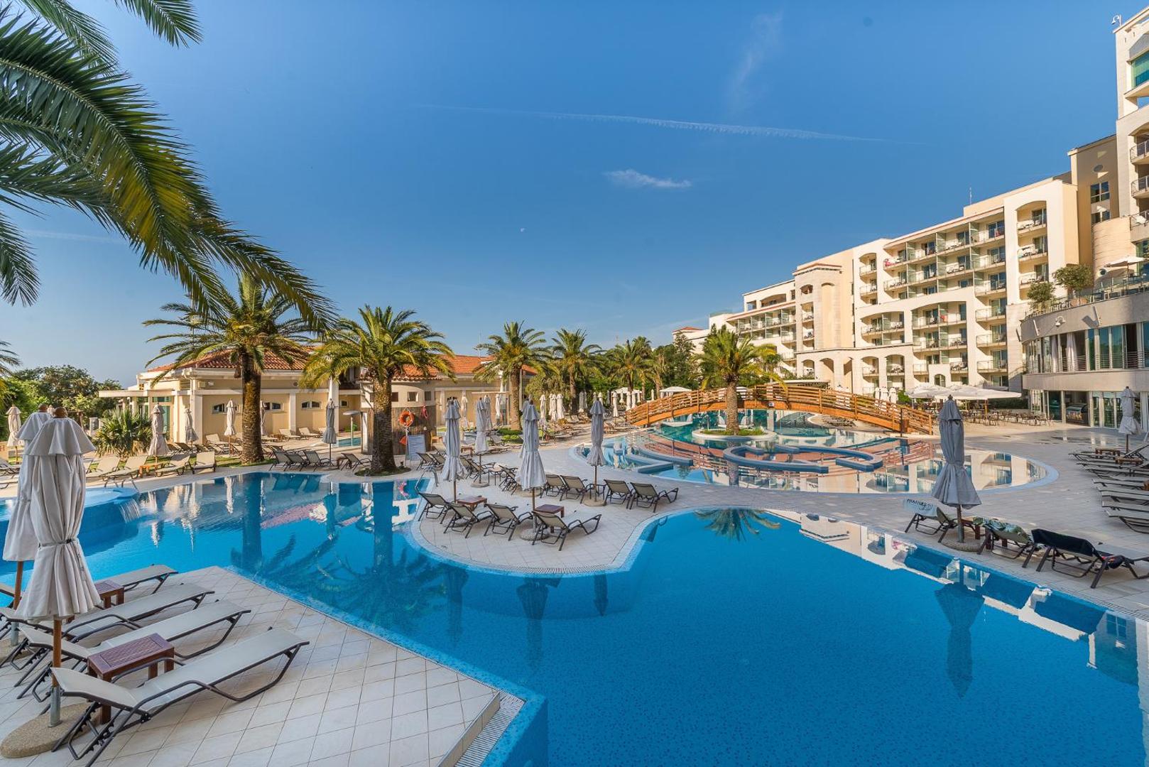 Splendid Conference & Spa Resort baseinu zona ar atpūtas krēsliem, palmām un viesnīcas ēku fonā saulainā dienā