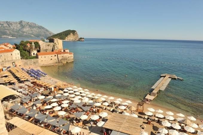 Plašs skats uz Avala Resort & Villas piekrasti, pludmali, piestātni un Budvas vecpilsētas cietoksni