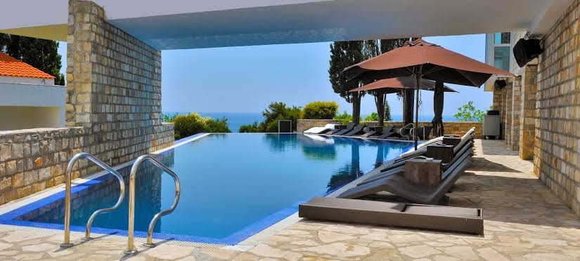 Avala Resort & Villas āra baseins ar atpūtas zonu zem saulessargiem un skatu uz piekrastes zaļumiem un jūru