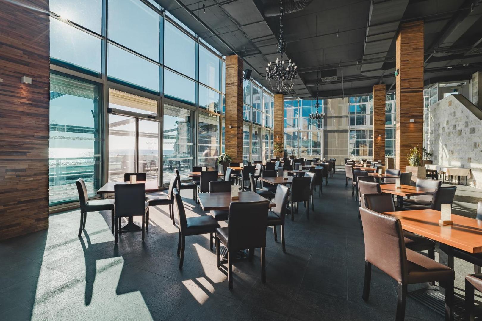 Avala Resort & Villas restorāns ar augstiem griestiem un panorāmas logiem — skats uz Adrijas jūru un āra terasi