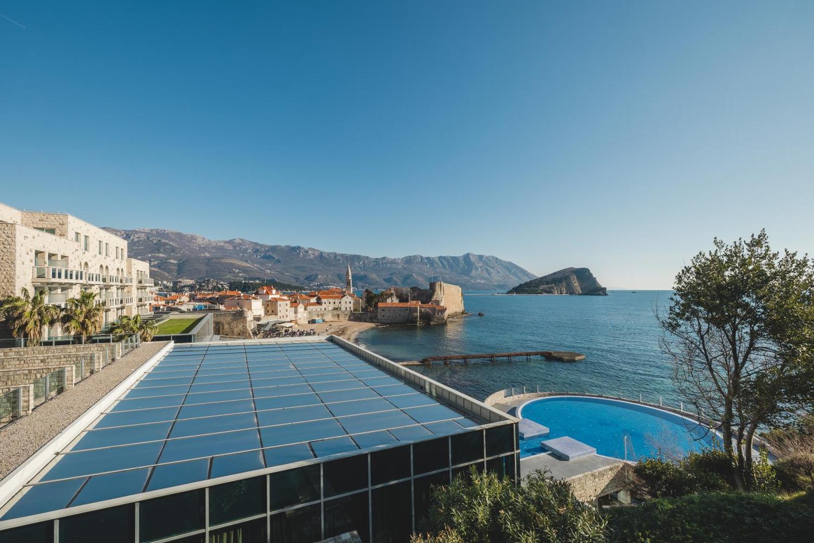Skats no Avala Resort & Villas terases uz Budvas vecpilsētu, jūru un kalniem — panorāmas skats ar baseinu un piekrasti