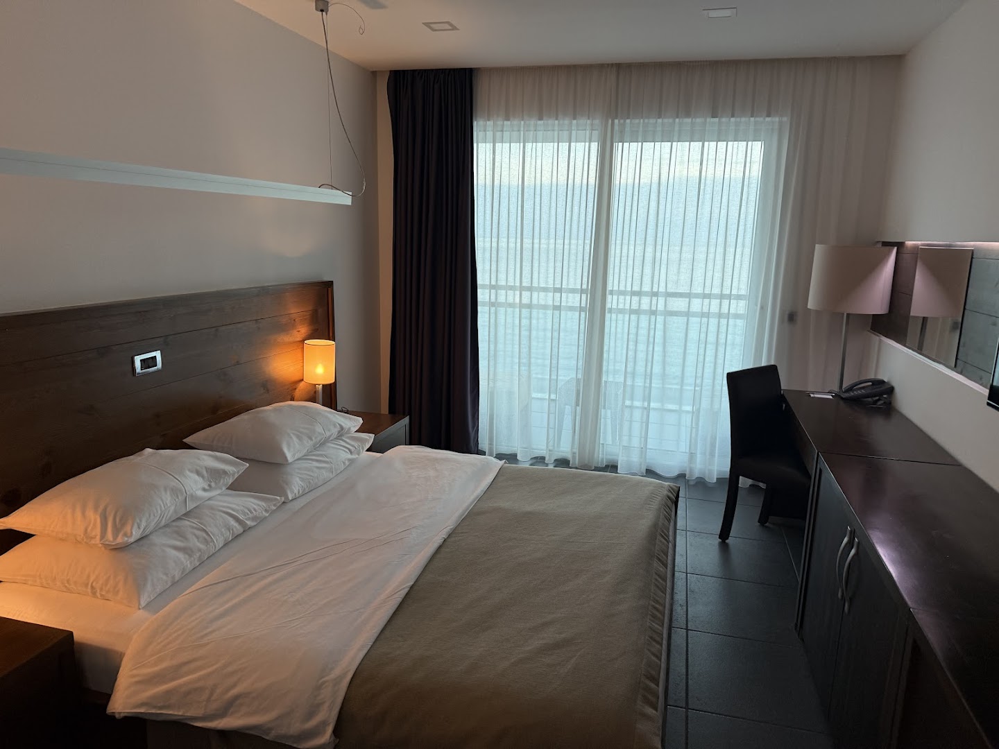 Avala Resort & Villas mājīgs numurs ar koka apdari, tumšām mēbelēm un lielu logu uz balkonu piekrastē
