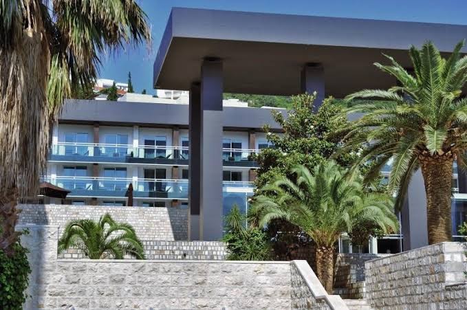 Avala Resort & Villas ieeja un fasāde ar palmām — moderni arhitektūras elementi un zaļā zona viesnīcas teritorijā