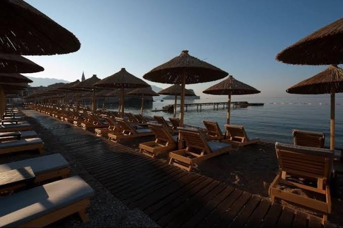 Avala Resort & Villas pludmales zona vakarā ar koka sauļošanās krēsliem un laipām pie klusas jūras