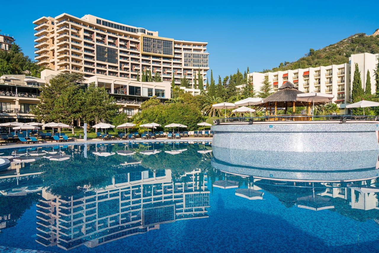 Iberostar Waves Bellevue viesnīcas ēka un liels āra baseins ar bāru, kurā atspoguļojas arhitektūra un zilās debesis
