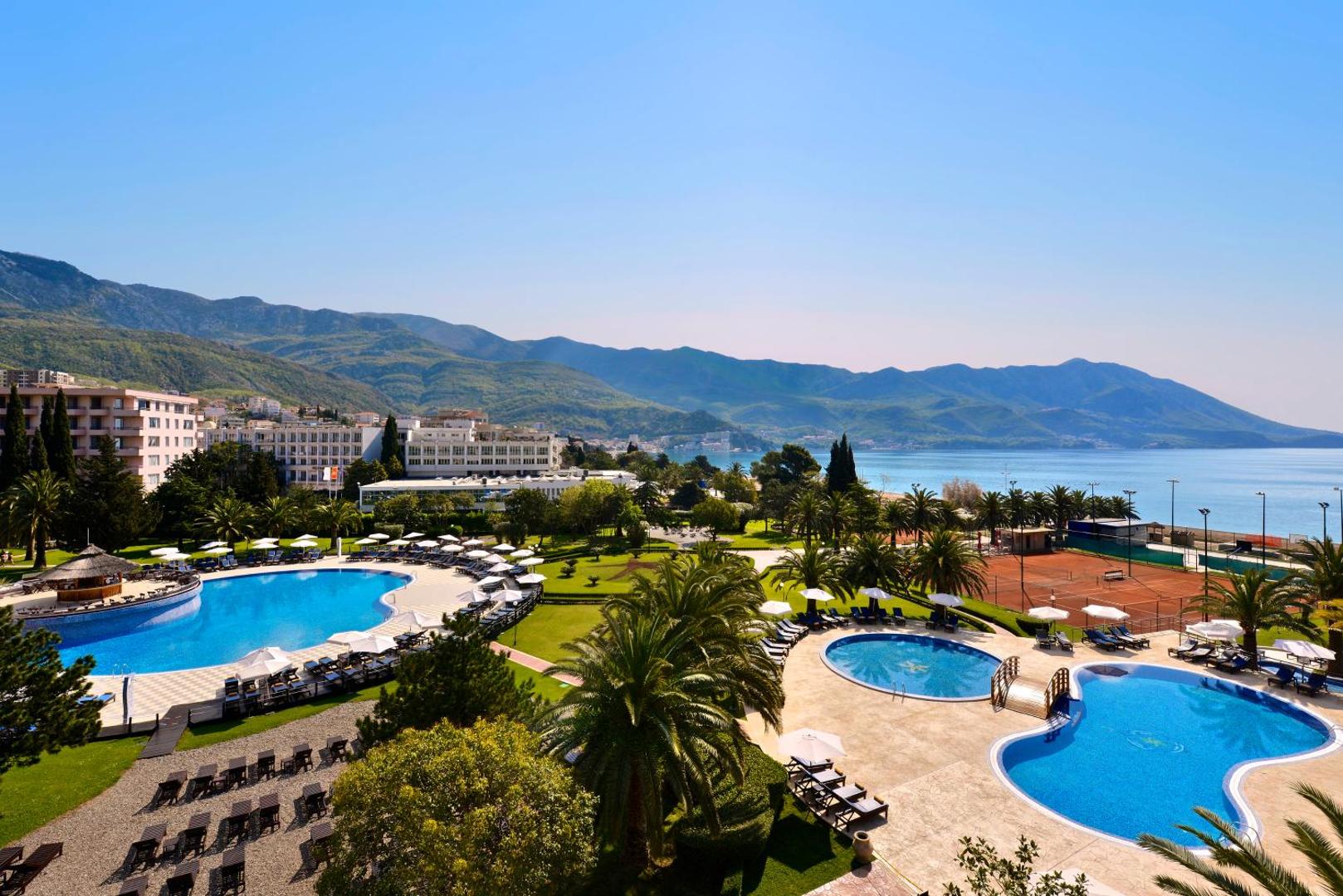 Iberostar Waves Bellevue viesnīcas teritorija no augšas ar vairākiem baseiniem, palmu dārzu, tenisa kortiem un jūras līci