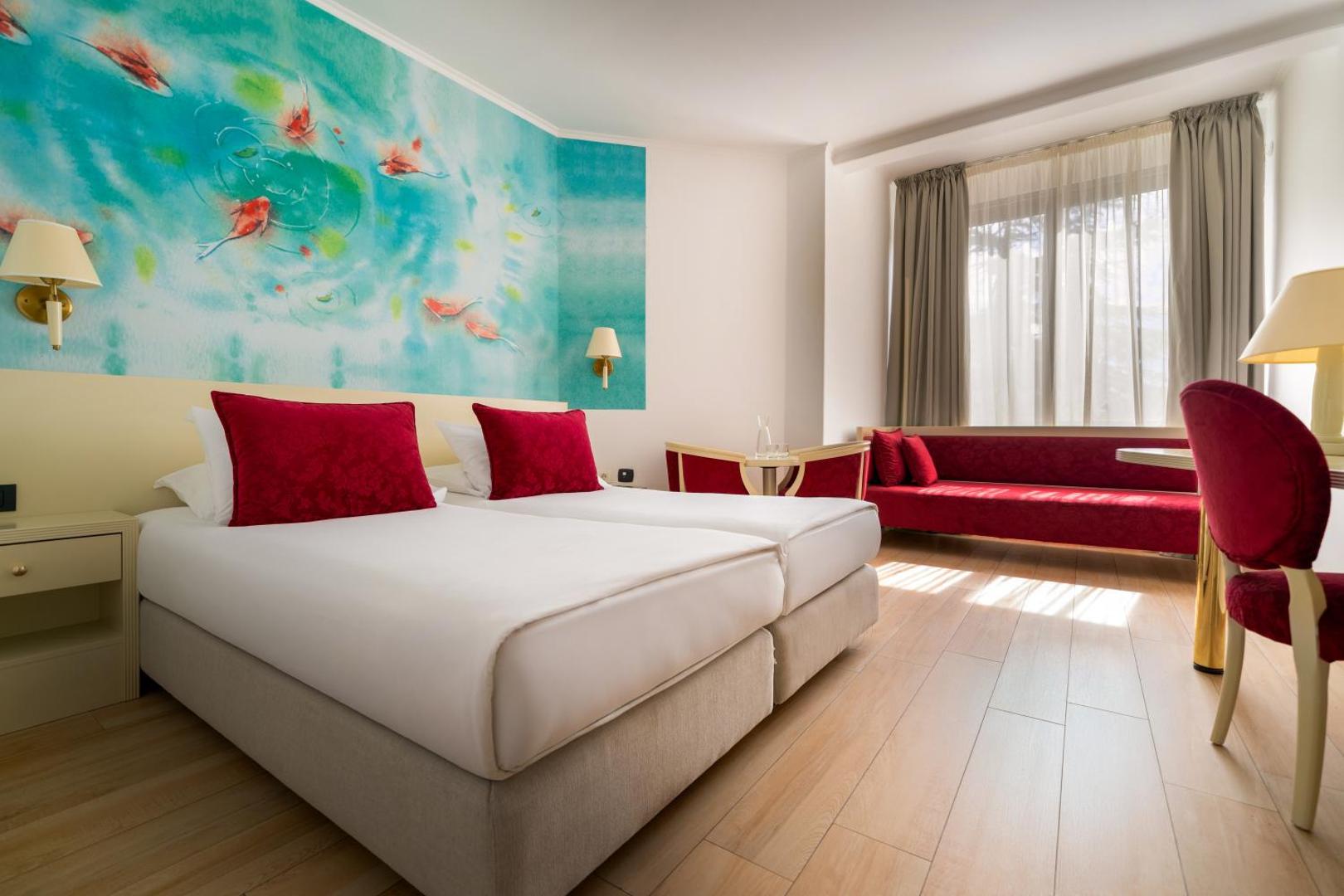 Iberostar Waves Bellevue gaišs viesnīcas numurs ar divām gultām, sarkanu dīvānu un māksliniecisku sienas gleznojumu ar zivīm