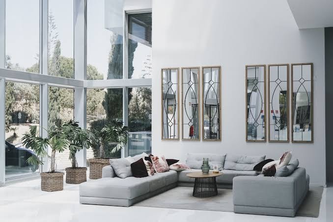 Gaiša un moderna Iberostar Waves Bellevue viesnīcas lobby atpūtas zona ar lieliem panorāmas logiem, mīkstajiem dīvāniem un dekoratīviem spoguļiem