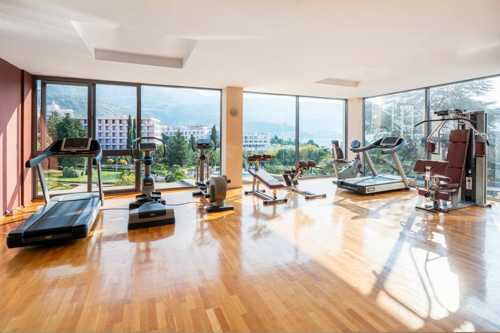 Iberostar Waves Bellevue modernā trenažieru zāle ar panorāmas logiem, skatu uz kalniem un dārzu Bečiči, Melnkalnē