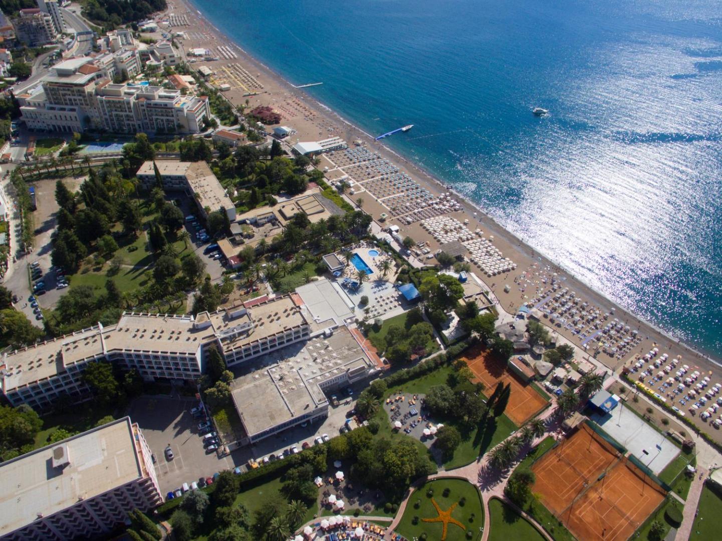 Montenegro Beach Resort panorāmas skats uz Bečiči pludmali un viesnīcas tenisa kortiem, baseiniem un saulaino piekrasti Melnkalnē