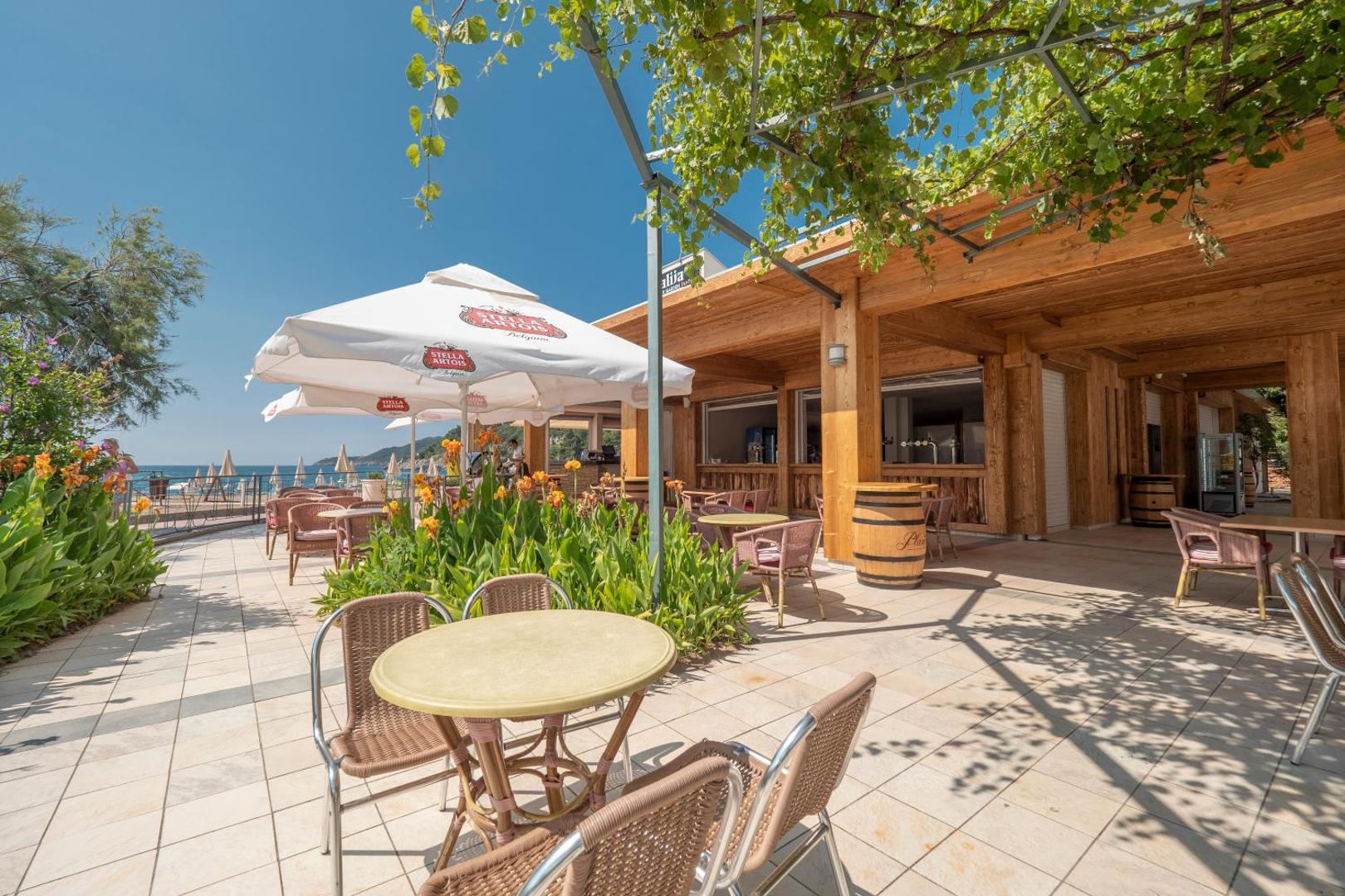 Montenegro Beach Resort pludmales bārs ar koka apdari, saulessargiem un ziedošām puķēm piekrastē