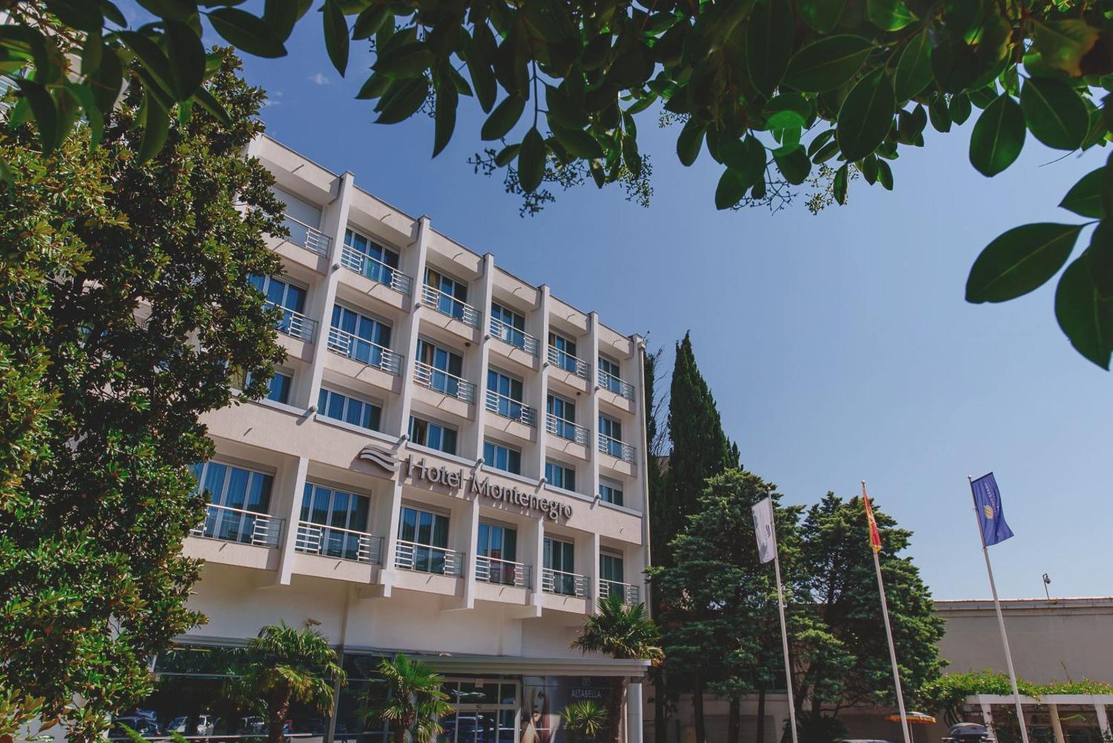 Montenegro Beach Resort galvenā ēka ar balkoniem un ieeju, ko ieskauj zaļi koki un palmas skaidrā dienas laikā