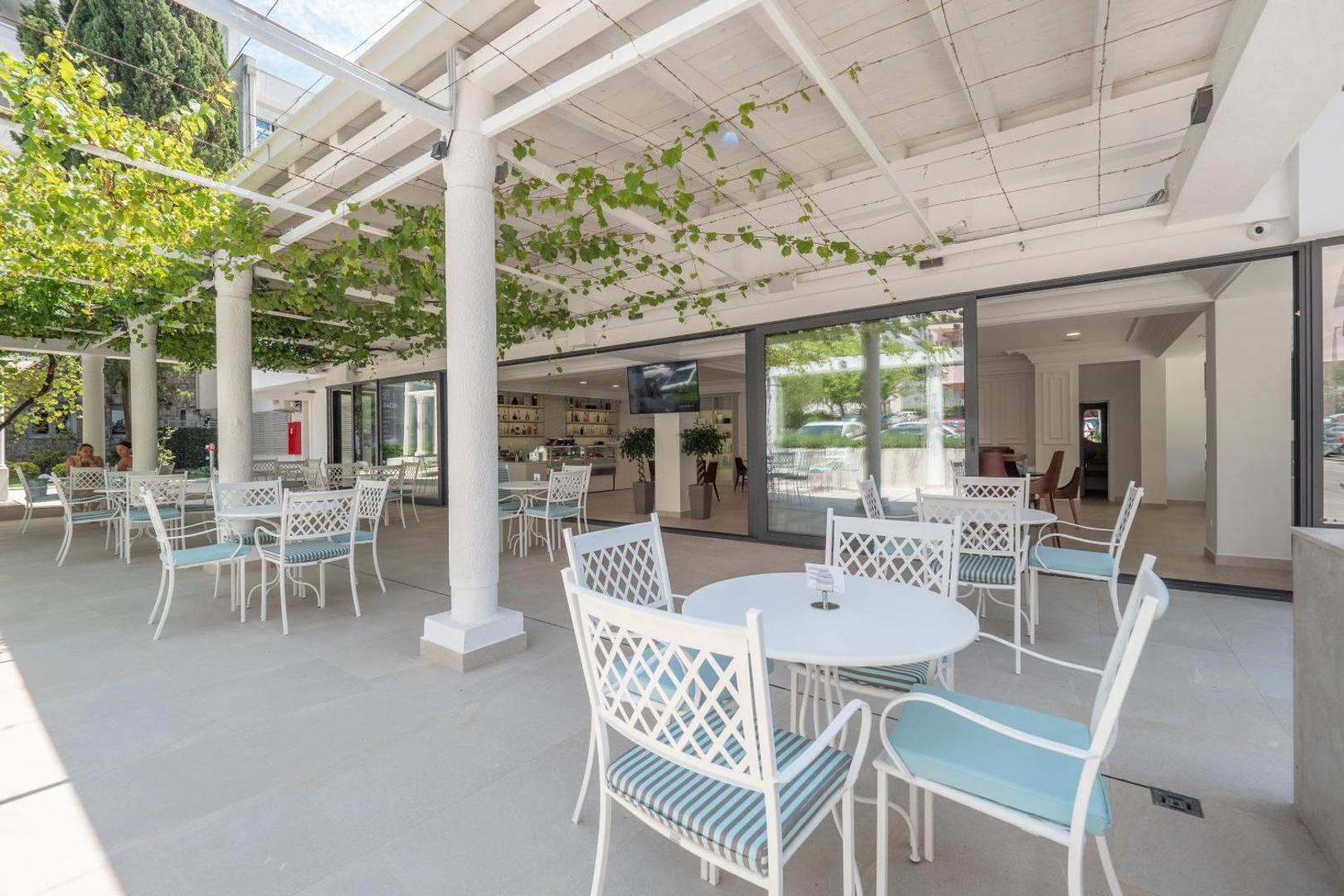 Montenegro Beach Resort āra terase ar baltām mēbelēm un vīnogulājiem klātu nojumi Bečiči kūrortā, Melnkalnē
