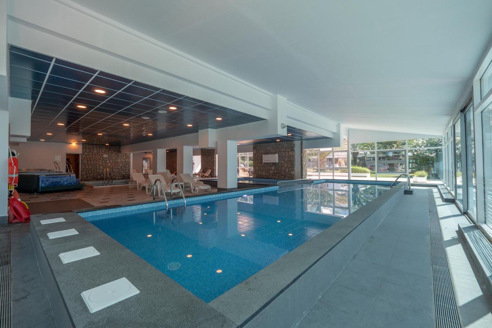 Montenegro Beach Resort iekštelpu baseins ar apsildāmu ūdeni, atpūtas krēsliem un lieliem logiem uz dārzu