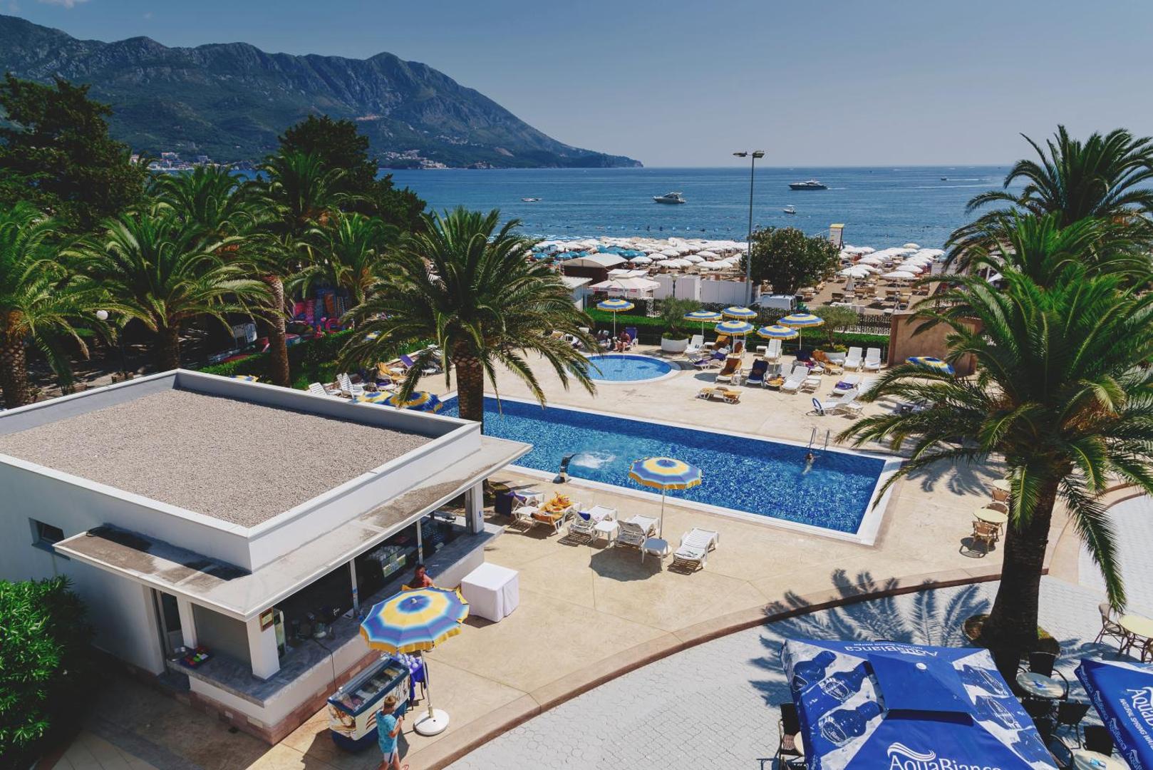 Montenegro Beach Resort āra baseins ar skatu uz Adrijas jūru un kalniem Bečiči kūrortā, Melnkalnē — palmas un sauļošanās zona