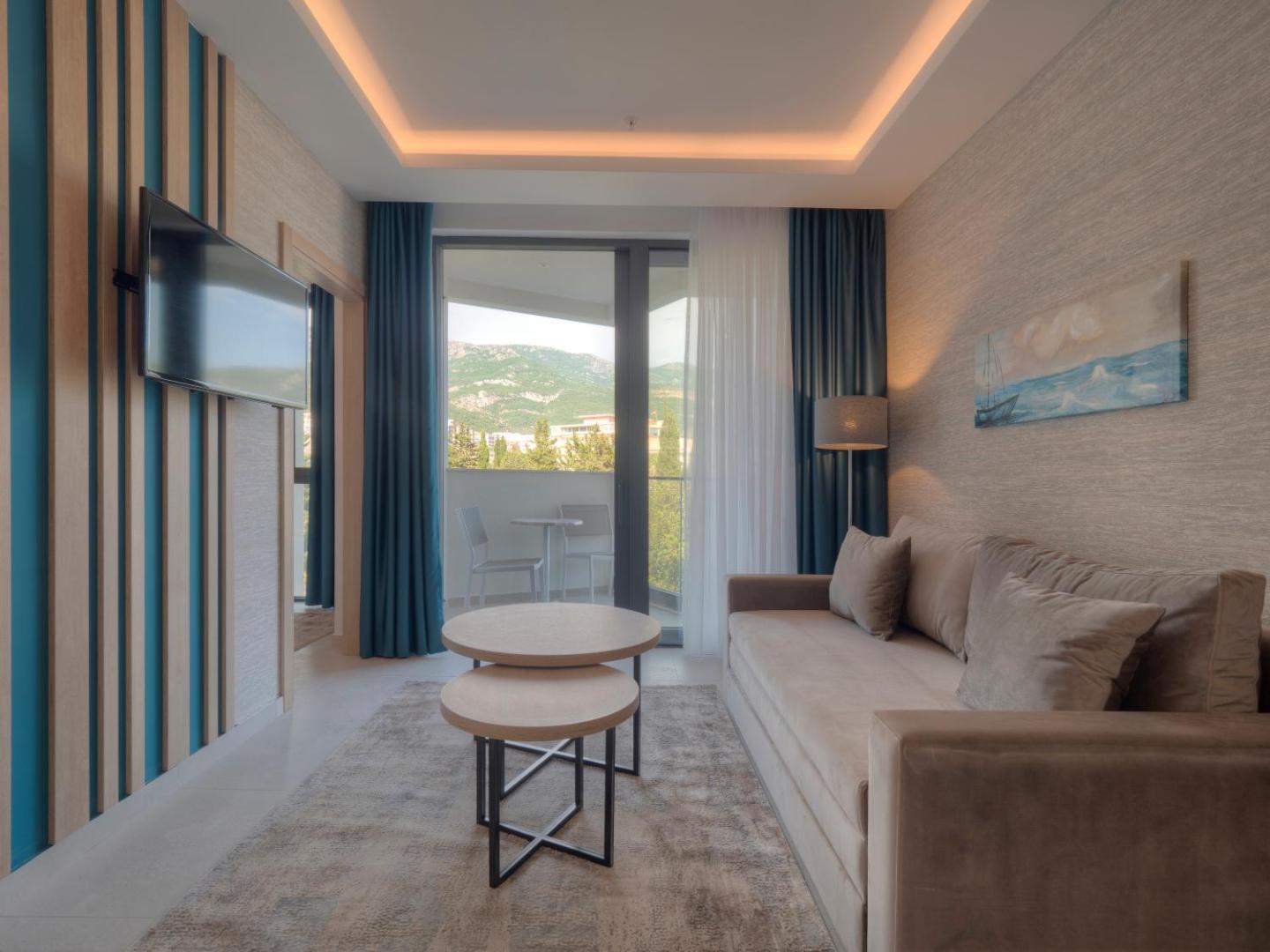 Montenegro Beach Resort moderns viesistabas numurs ar gaišu dīvānu, kafijas galdiņiem un balkonu ar skatu uz kalniem