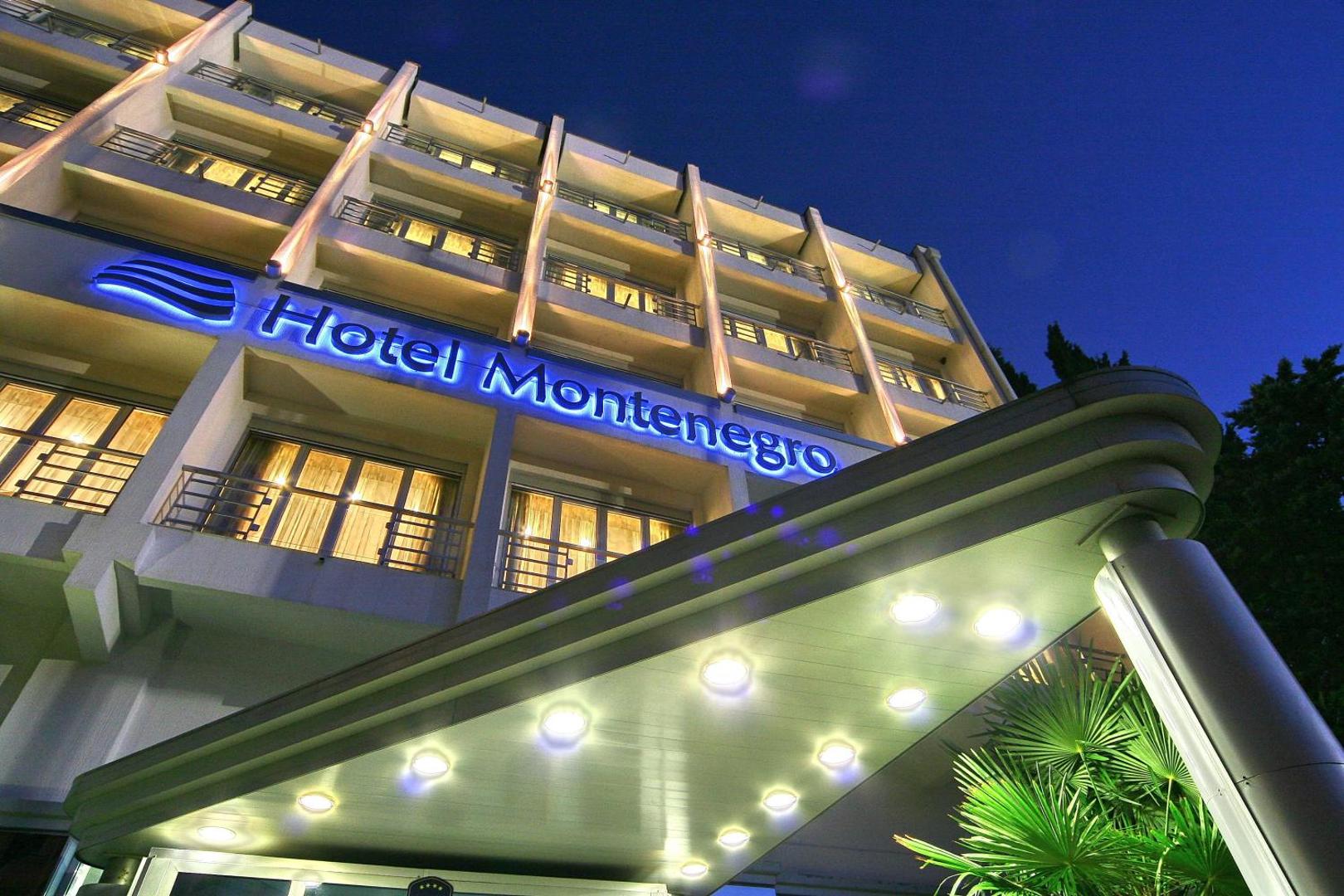 Montenegro Beach Resort ieeja un izgaismota izkārtne vakarā — moderna arhitektūra ar siltu apgaismojumu un palmu elementiem