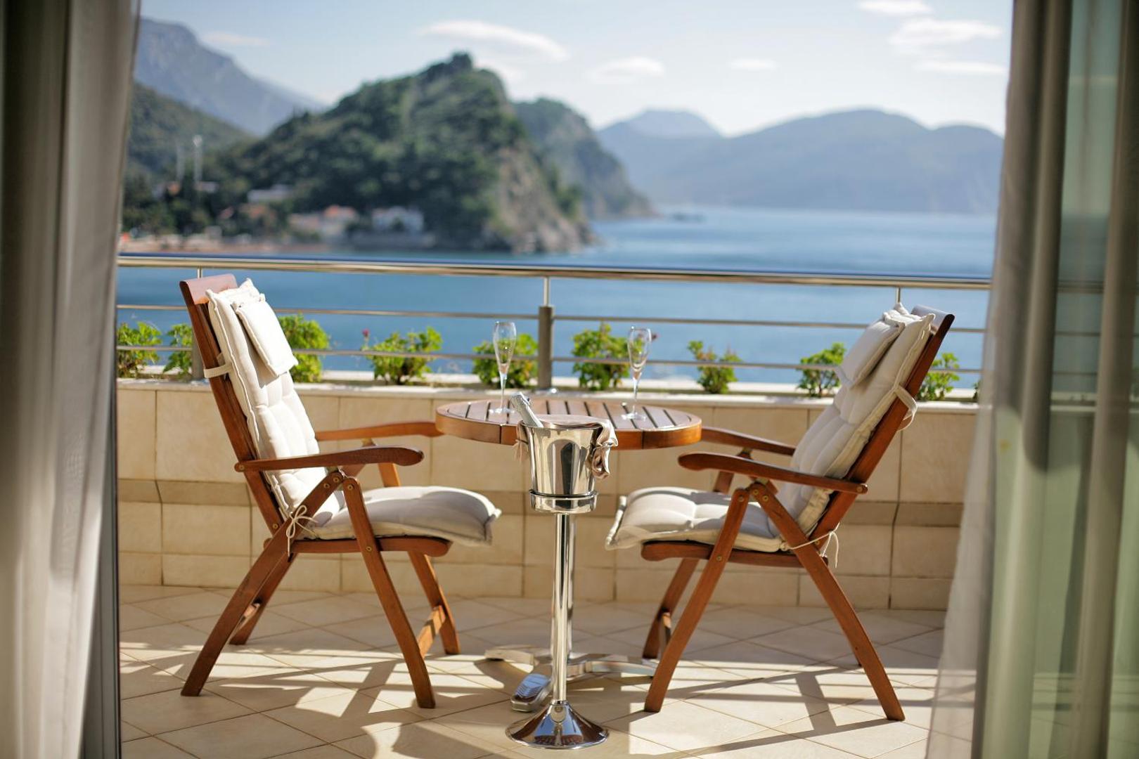 Romantiska atmosfēra uz Monte Casa Spa & Wellness numura terases — divi krēsli, galds ar dzērieniem un skats uz kalnaino piekrasti