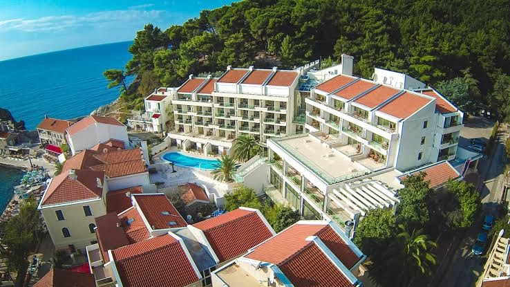 Monte Casa Spa & Wellness viesnīcas ēka Petrovacā, Melnkalnē — skats no augšas uz kūrorta kompleksu, āra baseinu un Adrijas jūras piekrasti
