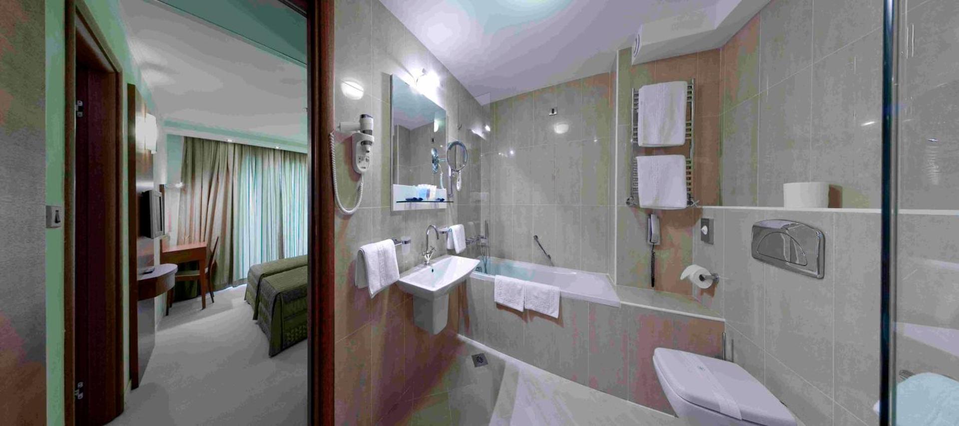 Monte Casa Spa & Wellness viesnīcas numura vannas istaba Petrovacā, Melnkalnē — gaišas flīzes, vanna ar stikla sienu, izlietne un fēns