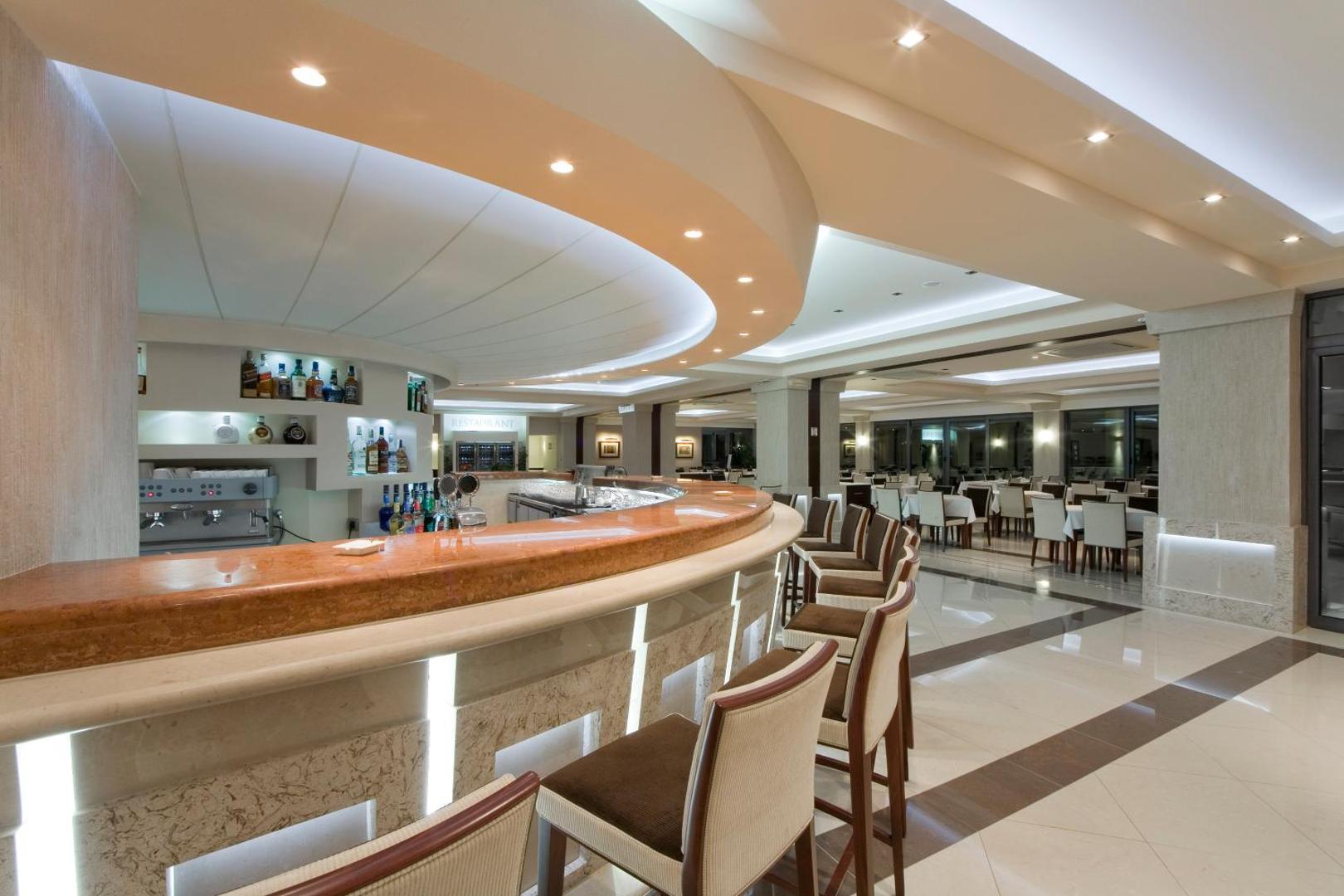 Monte Casa Spa & Wellness viesnīcas bārs ar marmora virsmu un elegantiem bāra krēsliem, fonā redzama plaša restorāna zāle