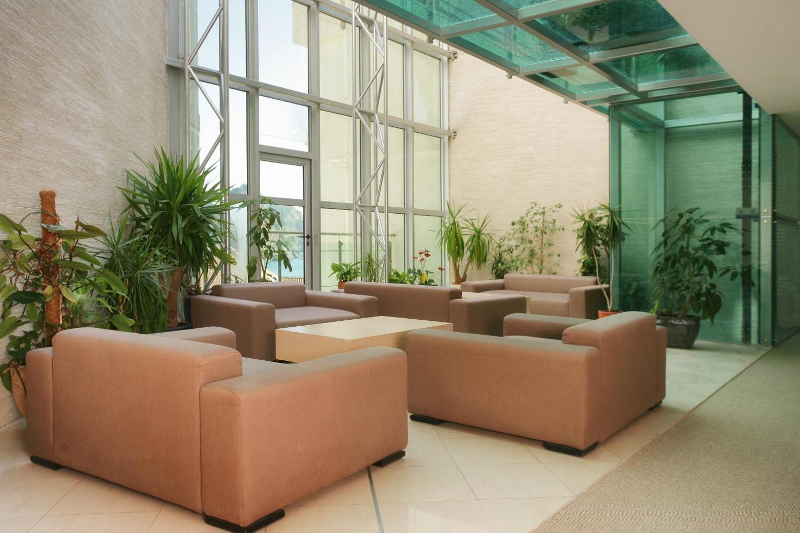 Monte Casa Spa & Wellness viesnīcas atpūtas zona ar gaišiem dīvāniem, telpaugiem un lieliem panorāmas logiem ar skatu uz jūru