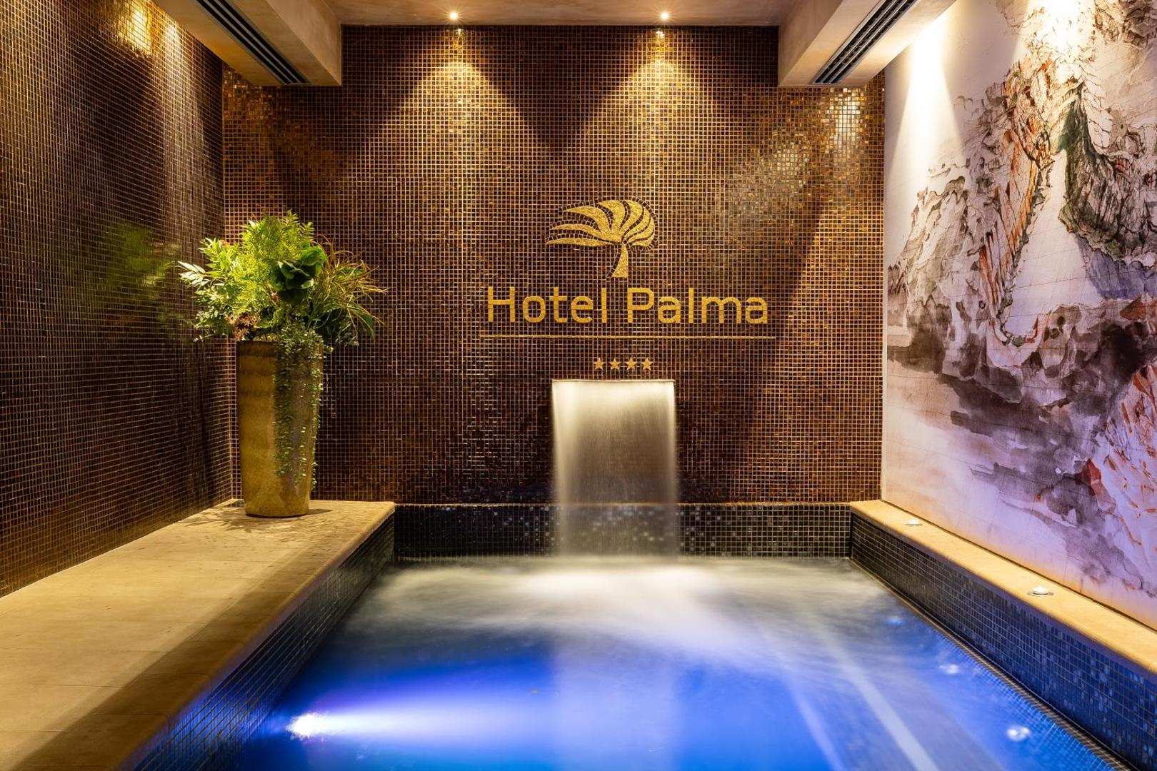 Hotel Palma spa zonas iekštelpu baseins ar dekoratīvu ūdenskritumu, mozaīkas flīzēm un viesnīcas logo uz sienas