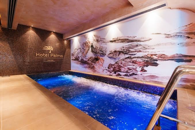 Viesnīcas Palma spa centrs ar iekštelpu baseinu, zilu apgaismojumu un dekoratīvu sienas gleznojumu