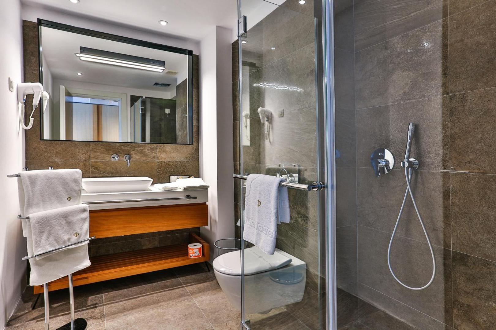 Moderna Hotel Fagus by Aycon numura vannas istaba ar stikla dušas kabīni, koka elementiem un lielu spoguli Budvā