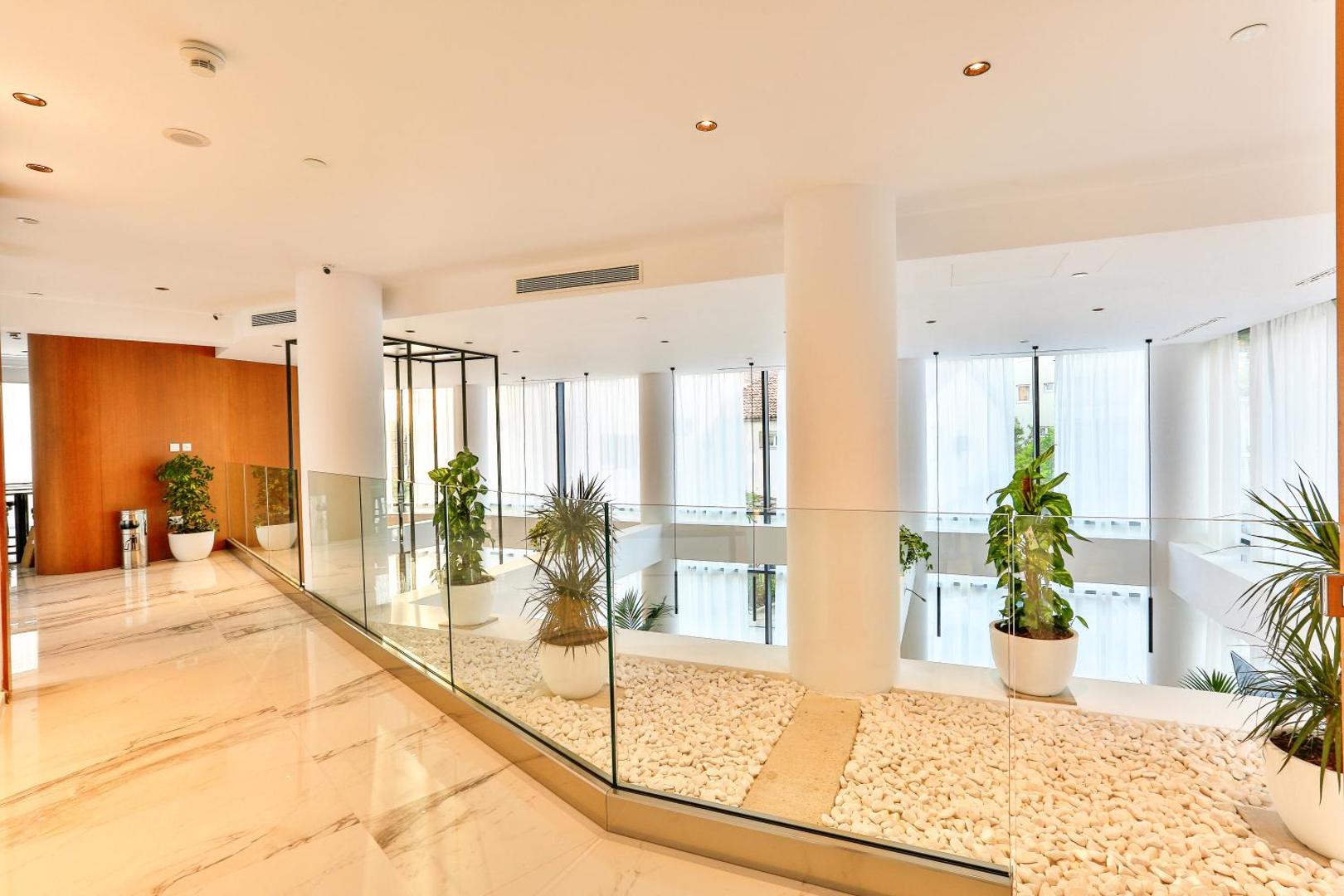Hotel Fagus by Aycon gaišais vestibils ar marmora grīdām, stikla margām un dekoratīviem telpaugiem baltos podos