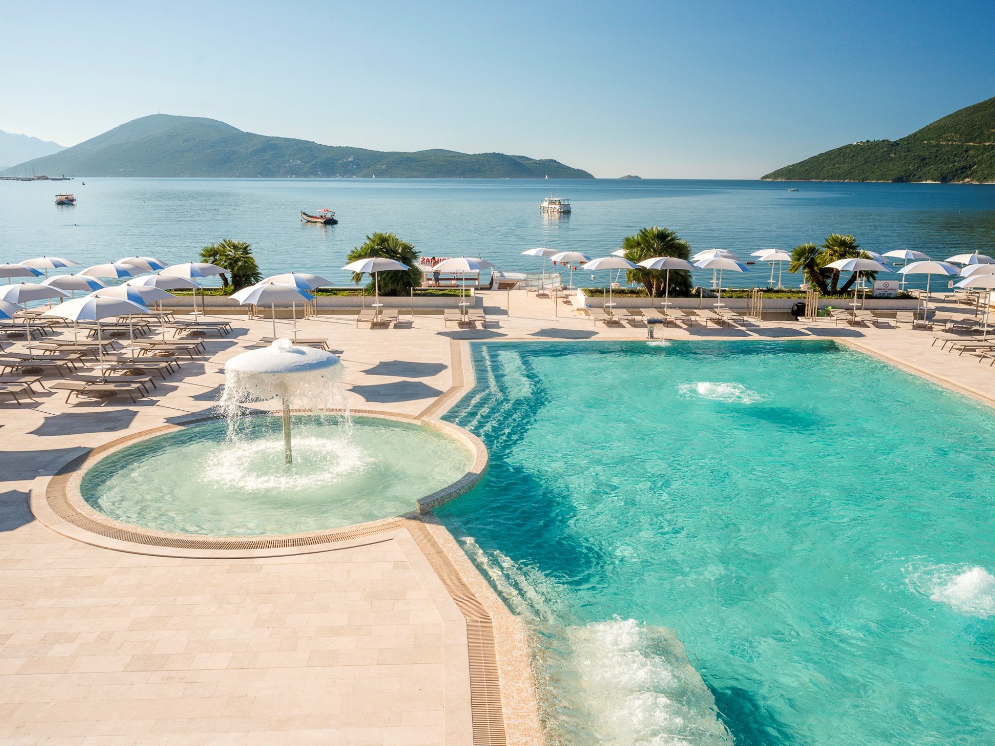 Palmon Bay Hotel & SPA āra baseina zona ar strūklaku, saulessargiem un panorāmas skatu uz līci un kalniem