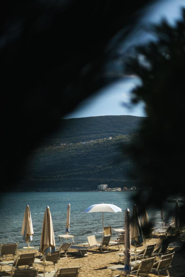 Palmon Bay Hotel & SPA privātā pludmale Melnkalnē ar saulessargiem un sauļošanās krēsliem, skats uz Kotoras līča kalniem