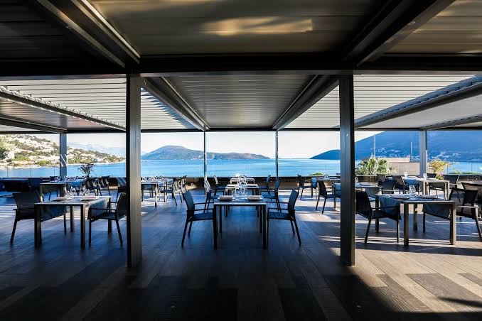 Plaša Palmon Bay Hotel & SPA restorāna terase ar modernām mēbelēm un stiklotiem norobežojumiem, paverot skatu uz līci