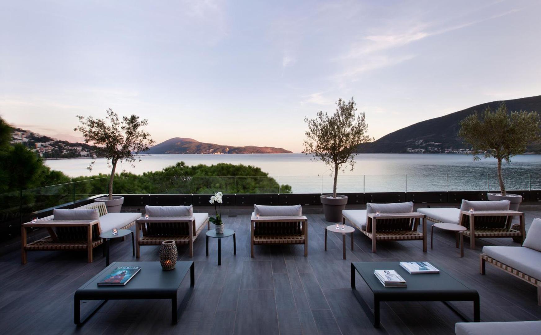 Palmon Bay Hotel & SPA āra terase ar atpūtas krēsliem un skatu uz jūru un kalniem saulrietā Melnkalnē