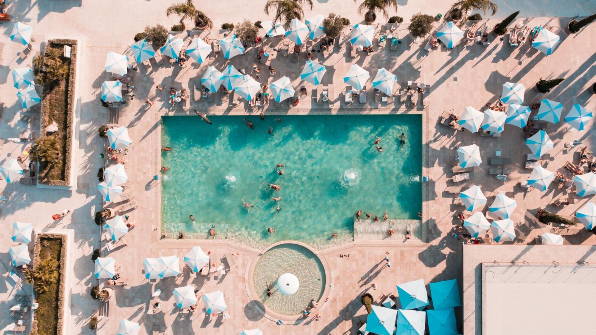 Aerofoto skats uz Palmon Bay Hotel & SPA āra baseinu, kurā redzami atpūtnieki un balti saulessargi