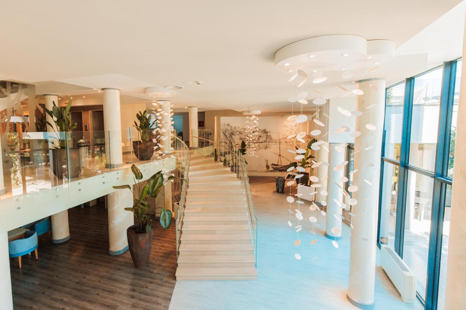 Palmon Bay Hotel & SPA modernais vestibils ar gaišām kāpnēm, dizaina gaismekļiem un dekoratīviem telpaugiem podos