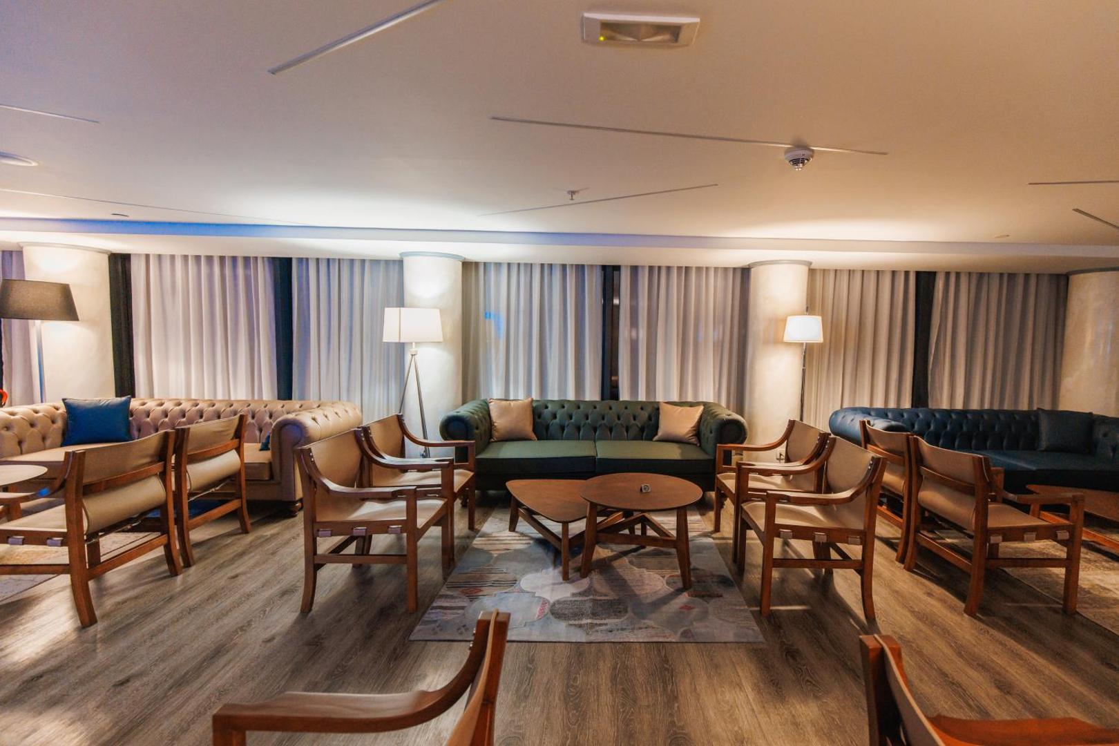 Mājīga atpūtas zona Palmon Bay Hotel & SPA lobby bārā ar mīkstajiem dīvāniem, koka krēsliem un siltu apgaismojumu
