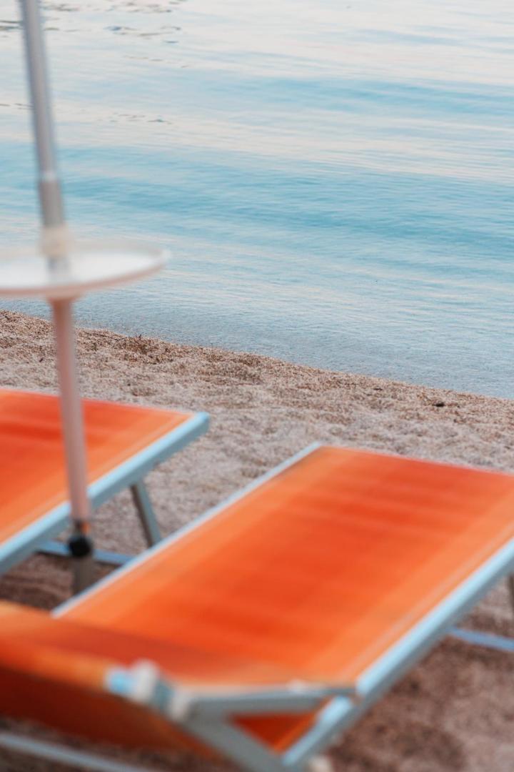 Tuvplāns ar oranžiem sauļošanās krēsliem Palmon Bay Hotel & SPA pludmalē pie dzidra Adrijas jūras ūdens Igalo kūrortā
