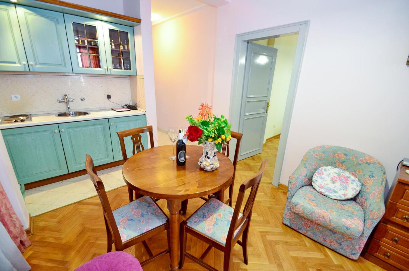 Villa Velzon numura virtuves zona ar gaiši zaļiem skapīšiem, pusdienu galdu un ziedu dekorācijām