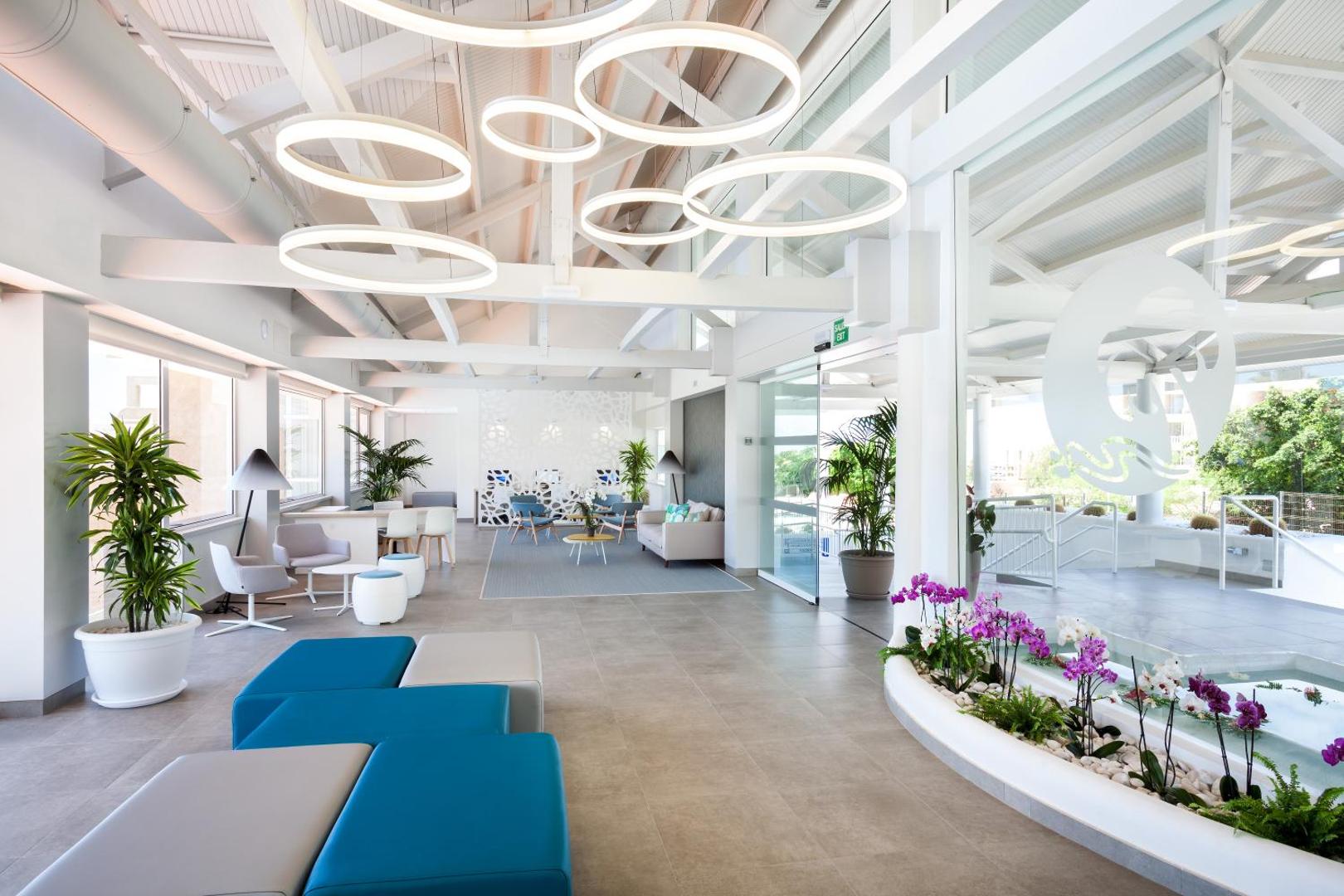 Tropical Park atpūtas zona lobby bārā ar stilīgiem ziliem dīvāniem, modernām lampām un plašiem logiem dienas gaismā.