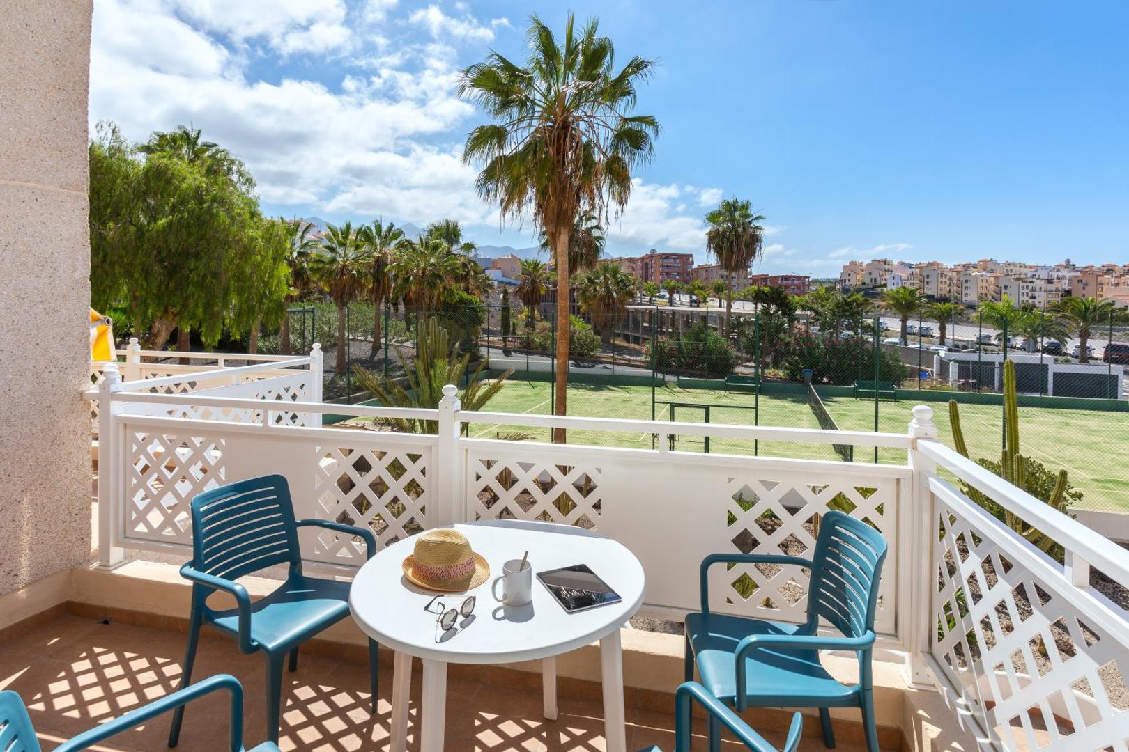 Tropical Park apartamentu privātais balkons ar galdu un krēsliem, no kura paveras skats uz tenisa kortu un palmām