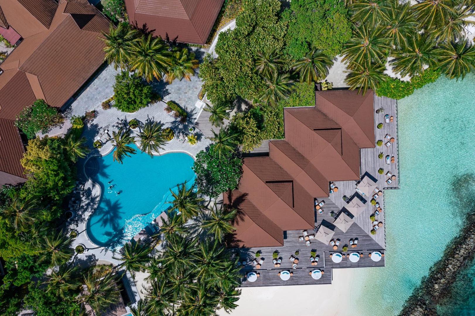 Niva Kurumba Maldives kūrorta skats no putna lidojuma uz āra baseinu, palmu dārzu un restorāna terasi pie okeāna krasta