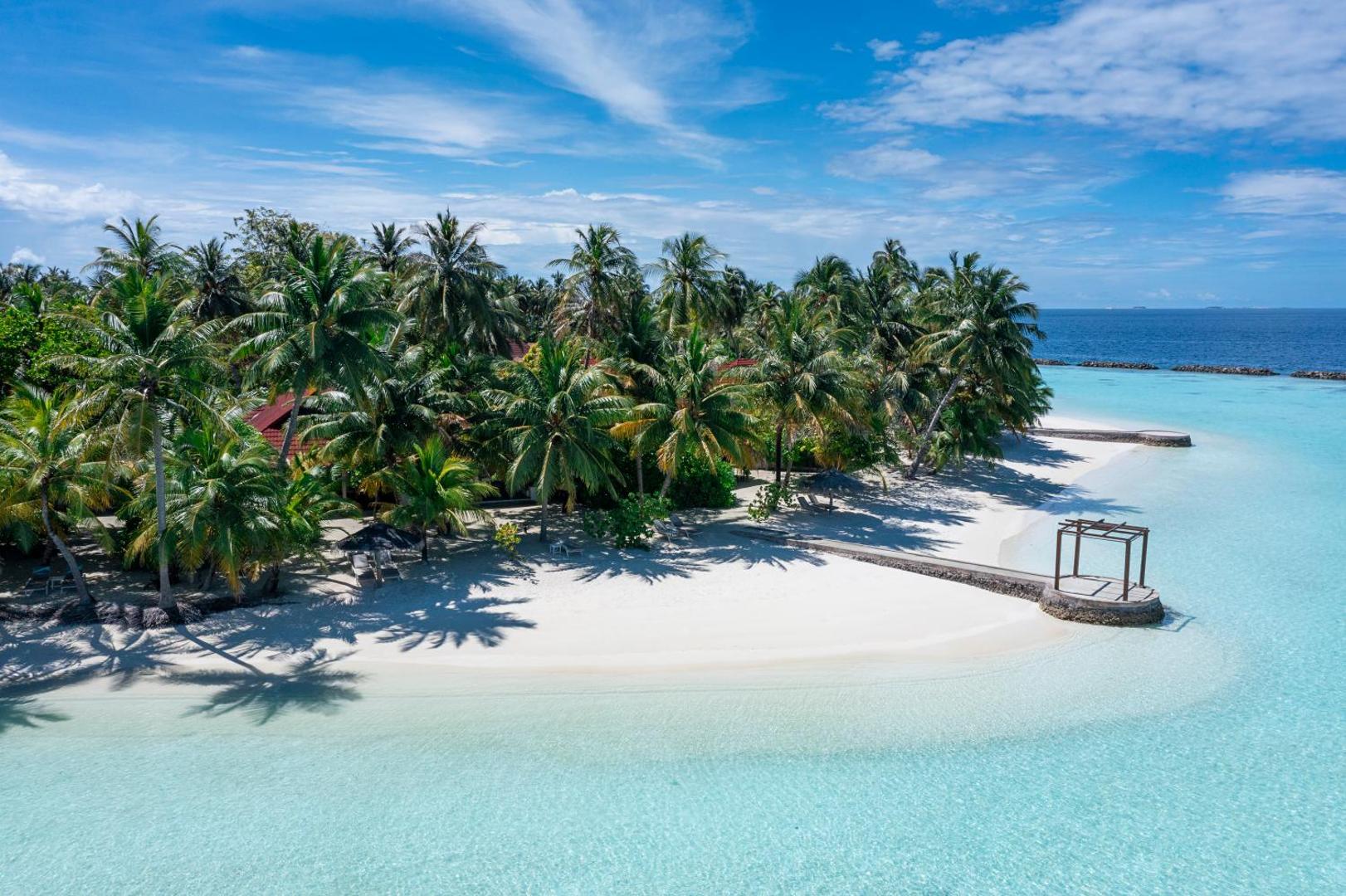 Aerofoto skats uz Niva Kurumba Maldives salu ar blīvu palmu mežu, baltu smilšu pludmali un koka laipu