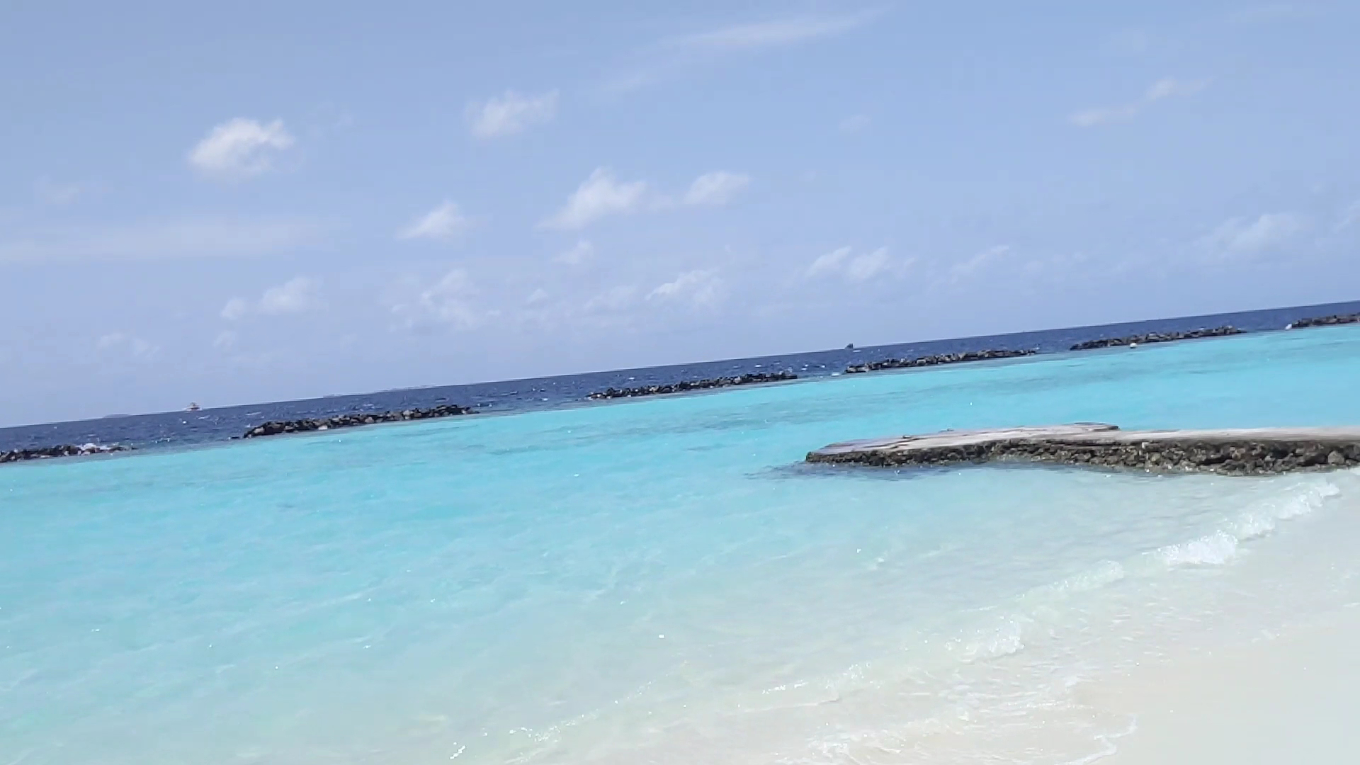 Niva Kurumba Maldives tirkīza krāsas okeāna ūdens un balto smilšu pludmales skats ar koka laipu tālumā zem skaidrām debesīm