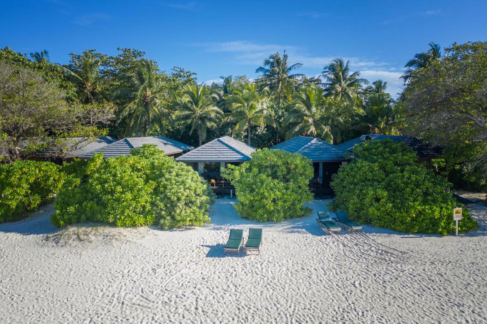 Royal Island Resort & Spa mājīgi bungalo pludmalē ar sauļošanās krēsliem smiltīs un kuplu tropu zaļumu fonā