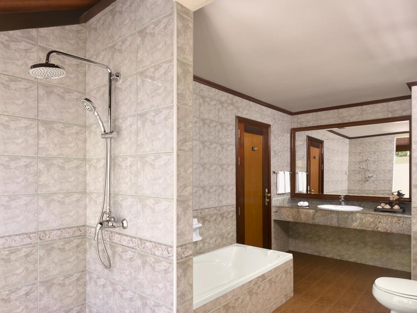 Royal Island Resort & Spa numura vannas istaba ar gaišām flīzēm, vannu, dušu un lielu spoguli virs akmens virsmas izlietnes
