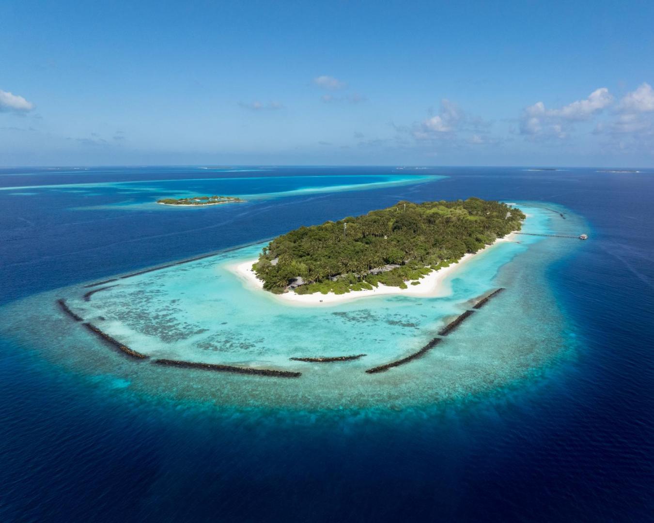 Royal Island Resort & Spa salas panorāmas skats no augšas Indijas okeāna vidū — zaļa sala ar baltām smiltīm un koraļļu rifu
