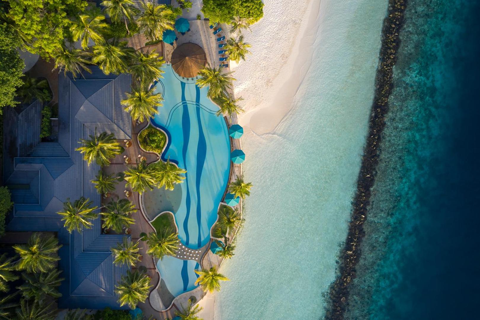 Royal Island Resort & Spa aerofoto ar baseina zonu, palmu dārzu un koraļļu rifu Maldivu salu piekrastē — skats no putna lidojuma
